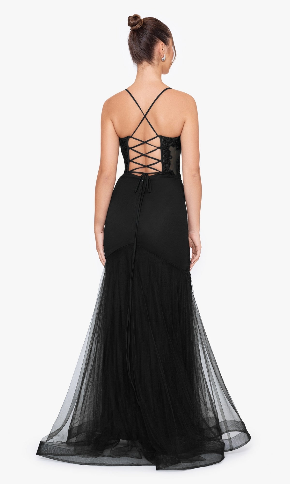A woman wearing the Blondie Nites Long Mermaid Prom Dress 3448BN, featuring a black corset-style waist, lace-up back, and tulle skirt, stands with her back to the camera against a plain white background.